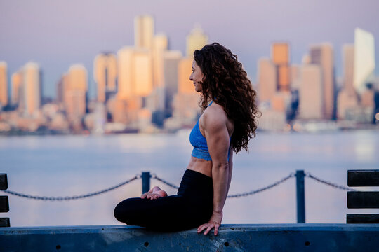 White woman practicing yoga by waterfront with Seattle skyline