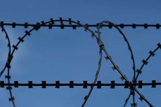 Close-Up of nato barb wire roll on a fence with blue sky and light clouds in the background