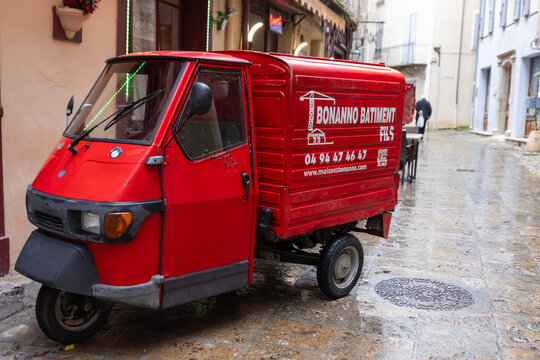 Entrevaux, France - December 26, 2025: A three-wheeled commercial van parked on a wet cobblestone street in the historic town.