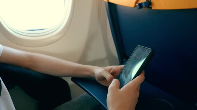 Unrecognizable traveler shopping online with smartphone during airplane flight. Hands browsing ecommerce products on mobile device. Digital consumer behavior and travel technology concept