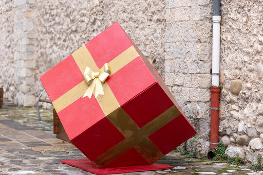 Entrevaux, France - A red gift box model with a gold ribbon sits on a cobblestone street against a stone wall.