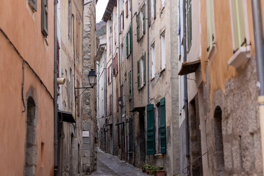 Entrevaux, France - : A narrow old street with shuttered buildings and wall lanterns in the historic town.