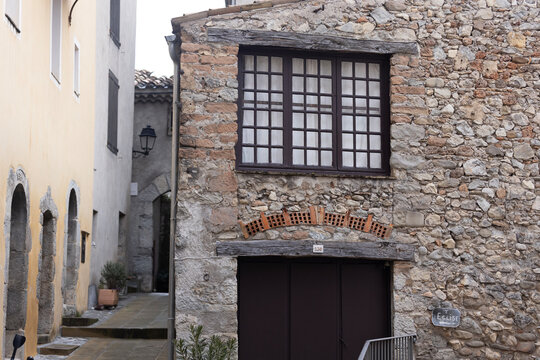 Entrevaux, France - , 2025: A stone house with a wooden window stands near a narrow street and an Eglise sign.