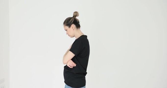 Anxious woman in simple black T-shirt walks around room. Female shows obvious nervousness through restless movements against white background