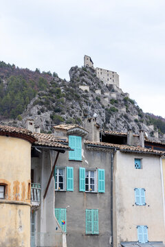 Entrevaux, France -  Colorful shutters and old houses sit below the hilltop citadel and rocky mountain of Entrevaux.