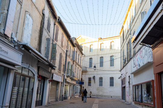 Arles, France - December 28, 2025: A narrow shopping street with local storefronts and hanging string lights in the old town.