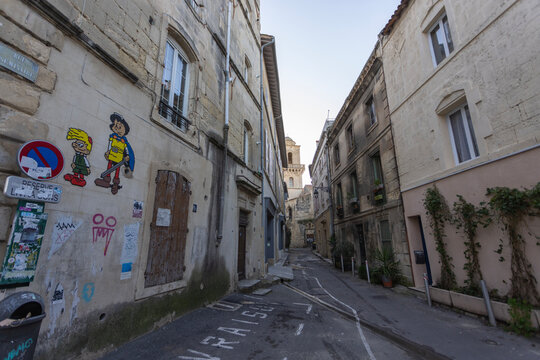 Arles, France -  A stone street corner with graffiti, posters, and street signs in the old town