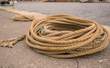 Heavy fiber mooring rope neatly coiled on a concrete pier in the port of Rijeka, Croatia. Marine dockage gear detail. © YuliiaKettu