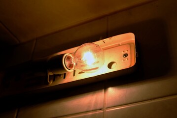 Glowing incandescent light bulb in an old vintage wall fixture illuminating a tiled wall in dim lighting © 이선 하