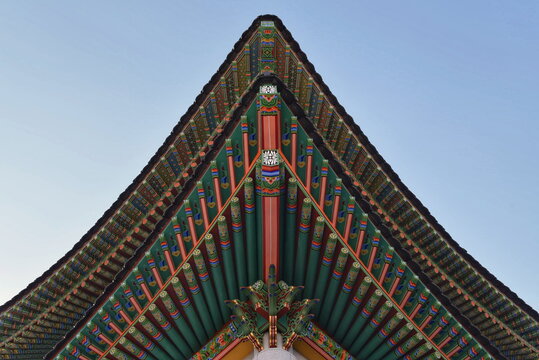 Symmetrical low angle view of traditional Korean Dancheong colorful painted wooden eaves and roof under clear blue sky, South Korea