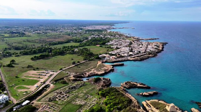 Aerial drone semi orbit revealing the rocky coastline, turquoise Adriatic Sea, coastal buildings and surrounding landscape of Roca Vecchia in Melendugno, Puglia, Italy.