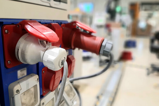 Industrial three-phase power plug closeup on blurred factory background. Heavy duty electrical equipment and plastic manufacturing concept.
