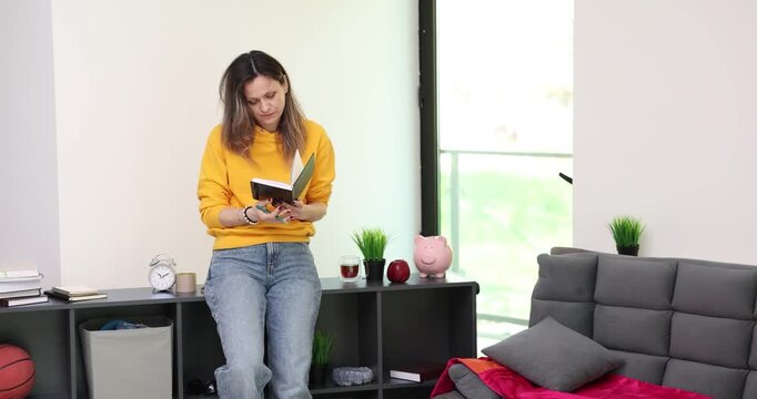 Young woman writes detailed list of daily tasks in notebook. Thoughtful female in comfortable casual clothes records plans for day in home office