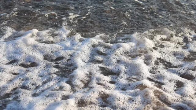 Slow-motion close-up of a small transparent wave rolling onto a pebble beach