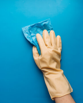 Yellow gloved hand wiping a blue surface with a blue cloth in vertical composition.