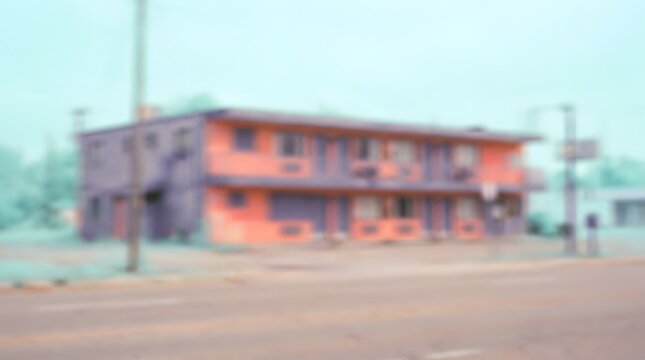 A vintage roadside motel under a hazy sky, with a weathered orange and purple facade and classic motel signs