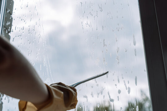 Gloved hand drawing a squeegee across the lower window amid wet cleaner trails.