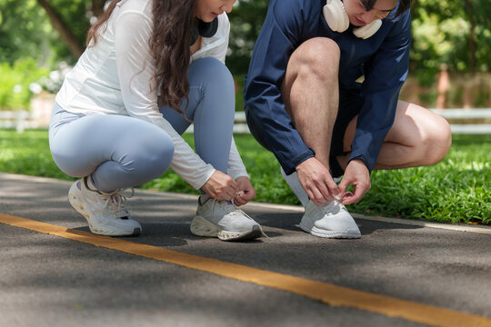 Asian couple tying running shoes on park track for outdoor fitness workout