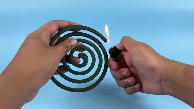 Hands Holding Spiral Mosquito Coil with Lighter on Blue Background