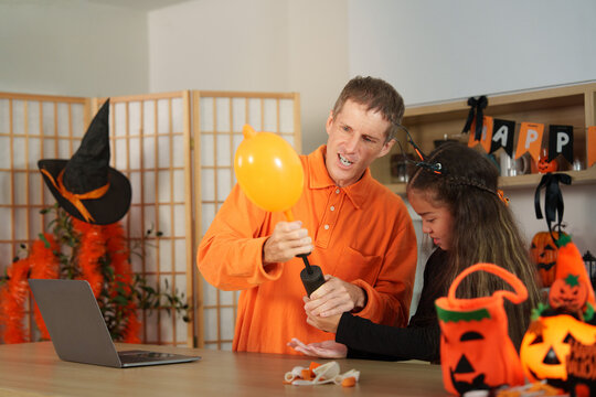 Father and daughter inflating orange balloon at home for Halloween party preparation