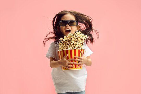 Cheerful Little Girl in 3D Glasses and Holding Popcorn Bucket Watch a Thrill Cartoon Movie Jumping with Popcorn that Flying to Asides Standing on Soft Pink Isolated. Movie Premiere. 