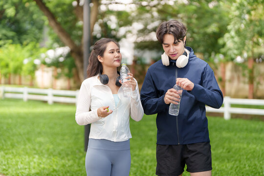 Asian couple holding water bottles in park for fitness exercise hydration break