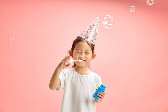 Cute Child Girl Blowing Soap Bubbles During Herself Birthday Standing on Pink Isolated