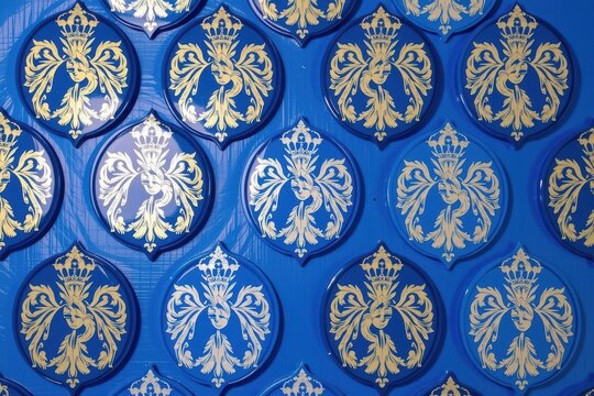 A classic ornamental damask repeating pattern of elaborate symmetrical feathered mask shields topped with ornate 1960s peace crowns in deep royal blue and silver.