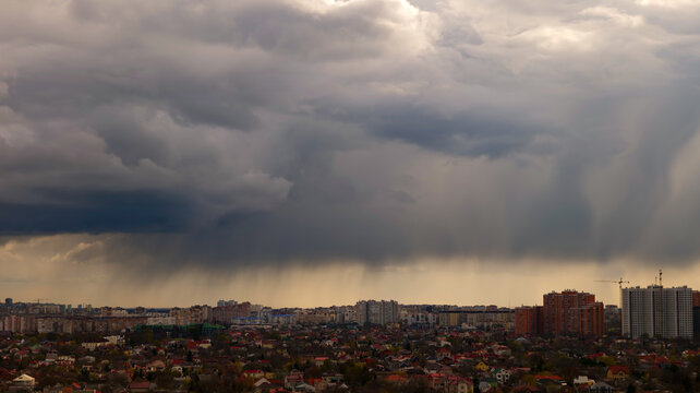 dramatic storm clouds with heavy rain shaft over city skyline panoramic view, dark overcast cloudscape with rain curtain over urban area, panoramic view of approaching storm and downpour over city