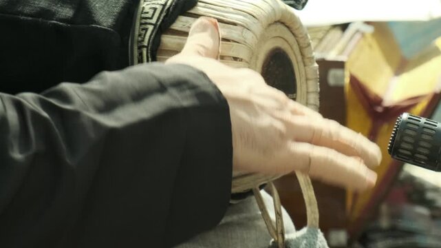 Musician hands playing mridangam drum with quick finger strokes across taut drumhead, performing changing rhythmic patterns on traditional Indian percussion instrument in close view of performance