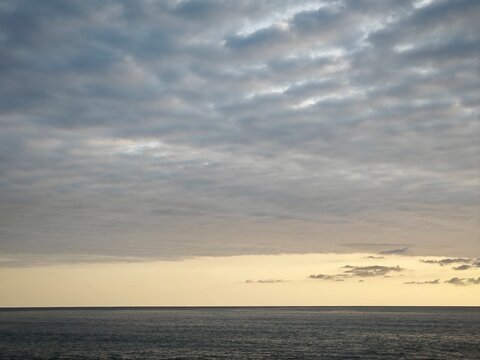 Overcast grey sky over the dark ocean at dusk. Seascape with a narrow band of yellow light at the horizon