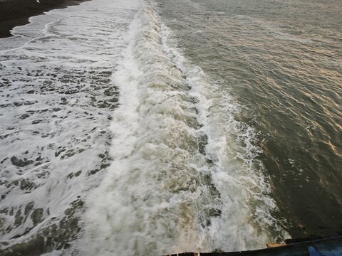 High angle view of ocean waves crashing on a dark sand beach. Foamy white water rolling towards the shore