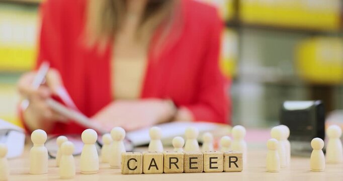 Ambitious female executive writes detailed ideas in small notebook. Decorative wooden cubes forming word Career stand on office desk. Slow motion