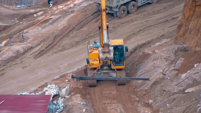 An orange hydraulic crawler excavator lifting steel rebar on a dirt construction site