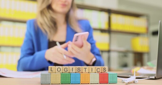 Businesswoman discusses terms of important product shipment with reliable partner over phone. Miniature wooden cubes form word Logistics at containers