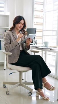 Professional business woman looking at online trade app. ASian woman holding digital tablet using  application at workplace in office.