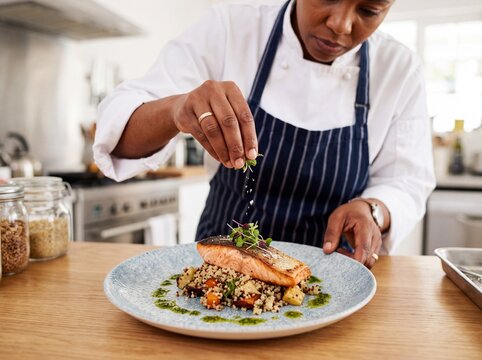 Professional chef garnishing grilled salmon dish in kitchen