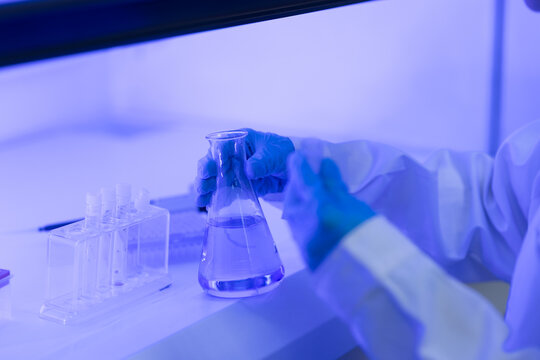 Laboratory research concept. scientist handles flask and test tubes inside safety cabinet for sample testing. laboratory, research, scientist, testing, science.
