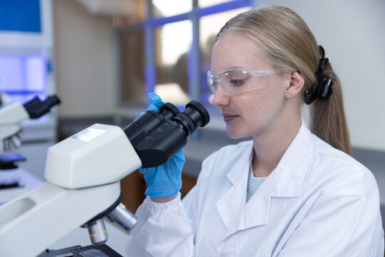 Medical research concept. female scientist examines specimen with microscope in laboratory while wearing protective eyewear. scientist, microscope, laboratory, research, science.