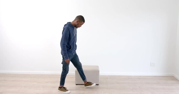 African American man sitting on stool in minimalist room, looking down thoughtfully