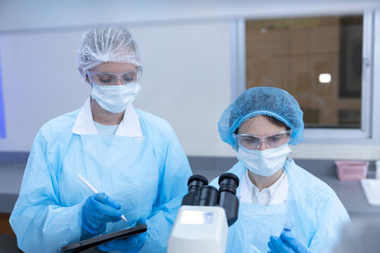 Women scientists working with microscope and tablet in laboratory for scientific research, biotechnology, medical analysis, microbiology, digital technology, laboratory safety and collaboration.