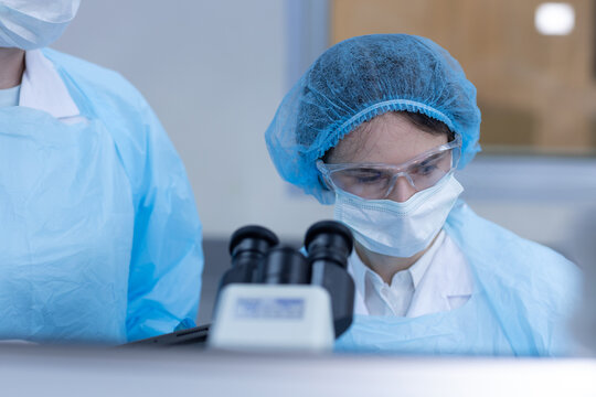 Women scientists wearing protective clothing working with microscope in laboratory for scientific research, microbiology, biotechnology, medical analysis, laboratory safety, healthcare innovation.