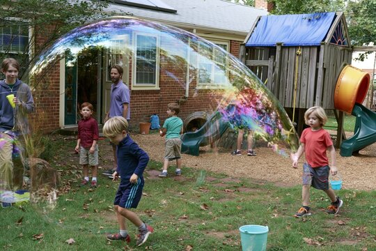 Children playing with giant soap bubble in backyard playground with family summer fun