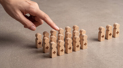 Fototapeta premium Close-up of a hand selecting a wooden figure from a crowd, symbolizing human resources, recruitment, leadership selection, talent management, and career choice in a professional business environment.