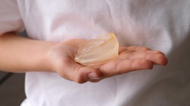 A child holds a holds a clear dental mouthguard in his hand close-up side view. Mouth aligner for bite, teeth and jaw correction. Orthodontic treatment, dental care, oral hygiene. HQ 4k footage.