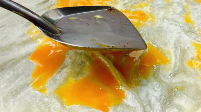 A chef spreading a fresh egg yolk over thin roti dough on a hot griddle pan. Concept of traditional Thai egg roti preparation, street food cooking process, and local culinary arts.