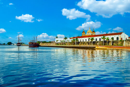 Vibrant harbor view of Cartagena, Colombia, featuring historic colonial architecture, ancient city walls, docked wooden galleons, and calm blue waters under a sunny sky.