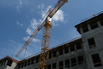 Fototapeta premium A powerful yellow tower crane is operating on a concrete structure under a clear blue sky. The concept of real estate investment, civil engineering, industrial progress, and urban development concepts
