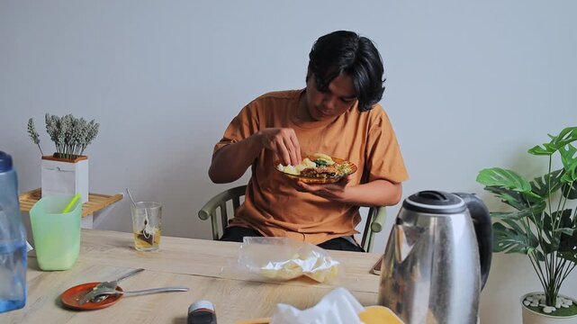 Young Man enjoying meal of padang rice and cassava leaves using hands at home