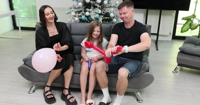 Cheerful father makes funny little dog figure from red balloon. Happy family enjoys lively and playful activity in cozy living room. Slow motion